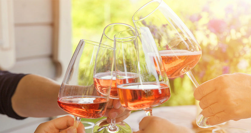 Vier Menschen stoßen mit Gläsern Roséwein in der warmen Nachmittagssonne an und feiern gemeinsam einen entspannten Moment im Freien.